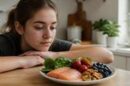 Adolescente con acné mirando un plato de comida saludable